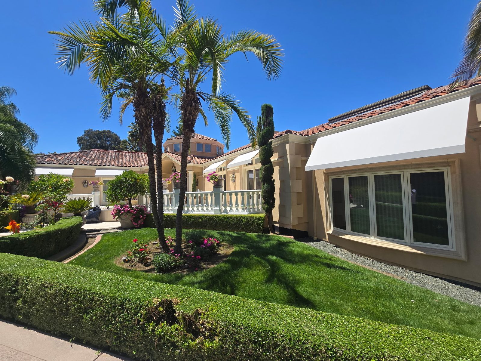 Mediterranean-style home with restored white door awnings, seen across a manicured lawn with palm trees