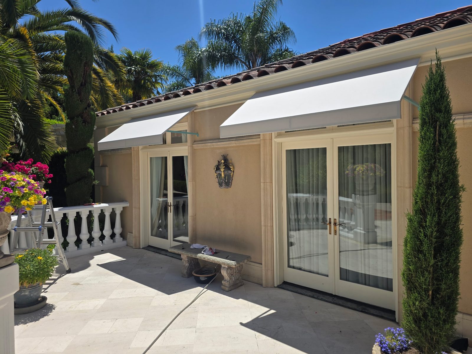 Two restored white awnings shading French doors along a stone patio