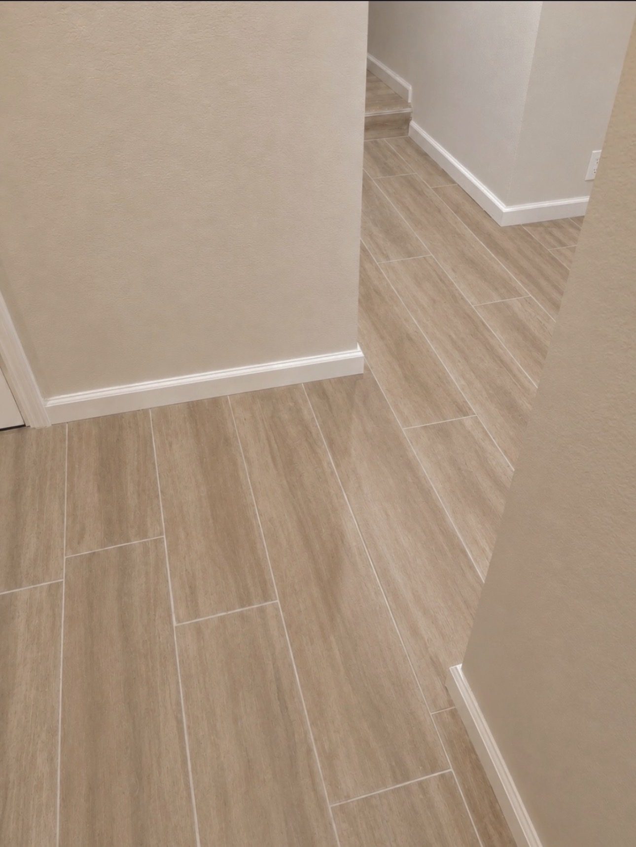 Wood-look plank tile flooring meeting white baseboards at a hallway corner