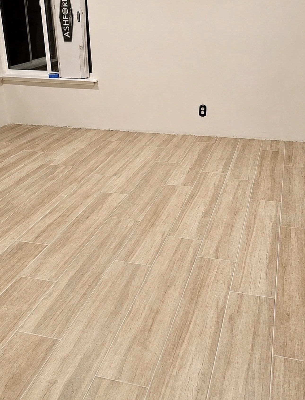 Wood-look plank tile flooring laid across an empty room beside a window