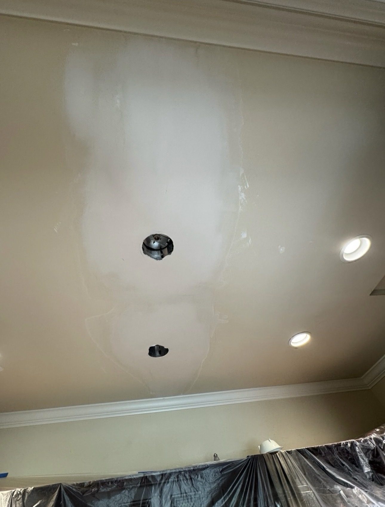Ceiling mid-installation, with patched and sanded drywall around a new recessed light opening and finished fixtures already in place alongside