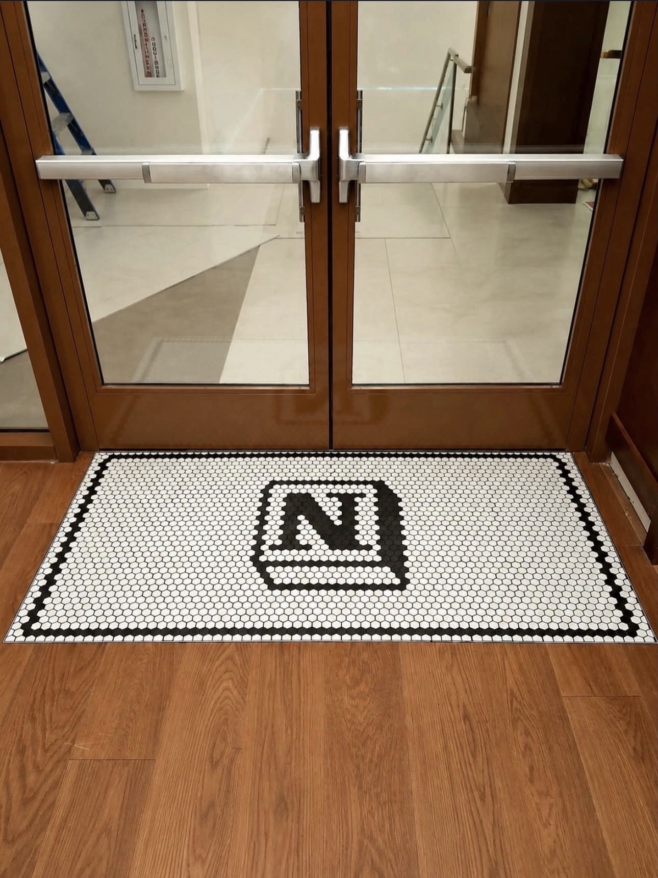 Black and white penny-tile mosaic entry mat with a custom monogram, set into hardwood flooring at glass entrance doors